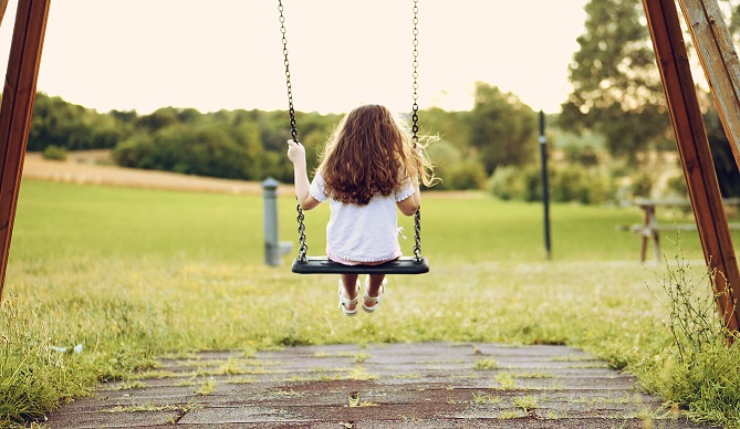 Back view of a little long-haired girl, swinging on a swing in a