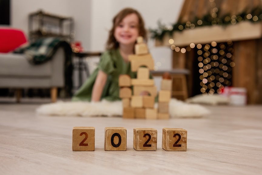 Wooden cubes with the numbers 2022 stand on the floor in a row. Background of a blurred happy girl