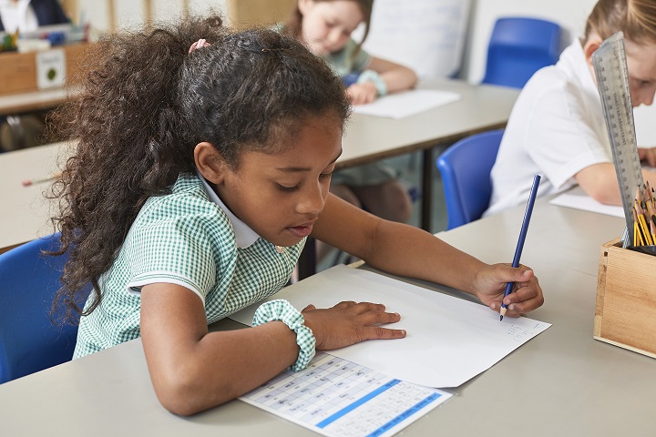 Schoolgirl writing at classroom desk in primary school lesson