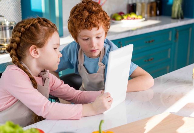 children in aprons using digital tablet while cooking together in kitchen