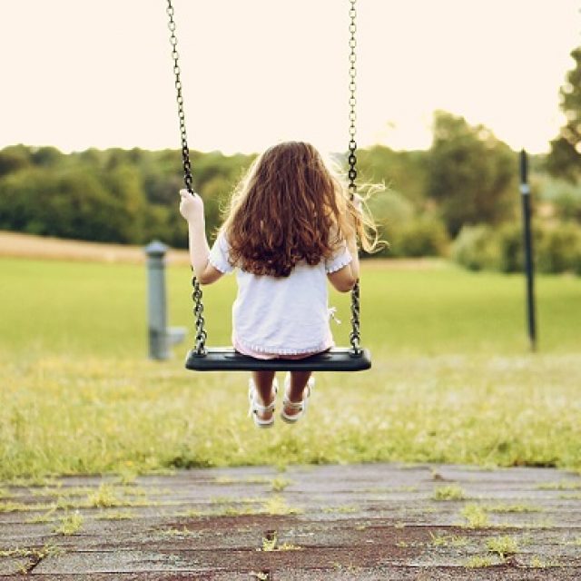 Back view of a little long-haired girl, swinging on a swing in a