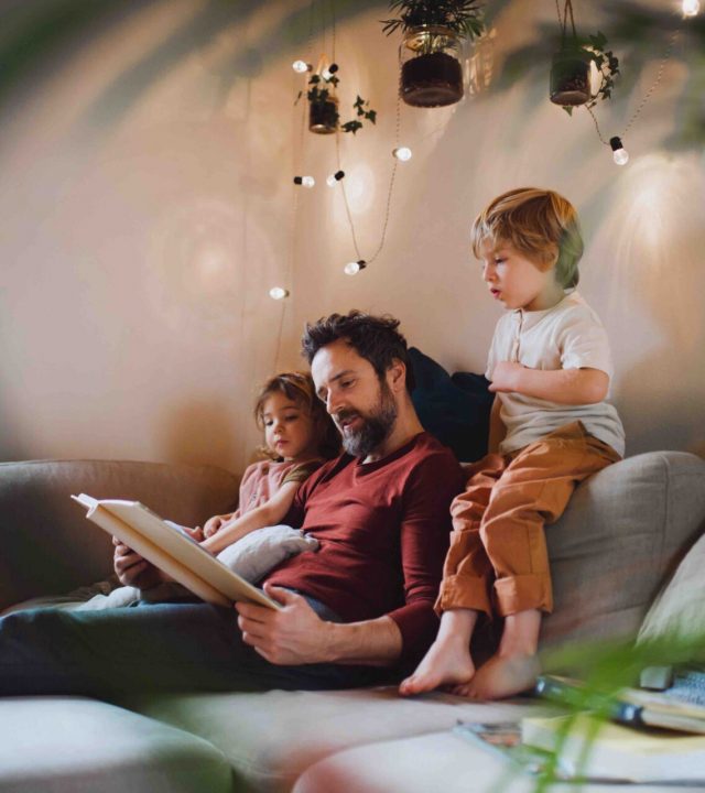 A mature father with two small children resting indoors at home, looking at photo album.