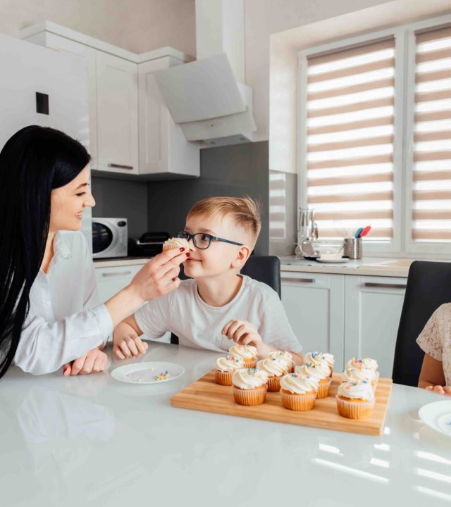 Mother treats little children with delicious cupcakes. Family sitting in the kitchen