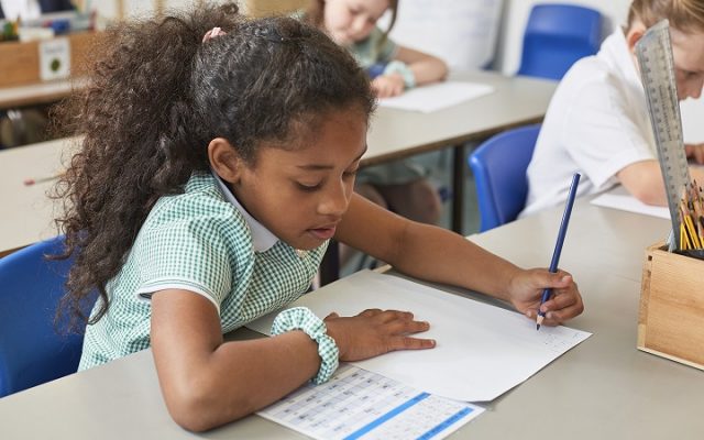 Schoolgirl writing at classroom desk in primary school lesson